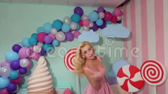 一个穿着粉红色条纹连衣裙的快乐女孩在大糖果背景上的肖像视频的预览图
