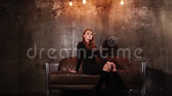 年轻优雅的女人坐在阁楼墙上的皮革沙发上视频的预览图