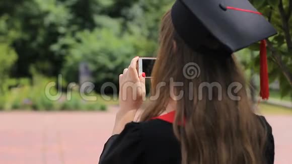 戴着毕业帽的女性在公园的智能手机上为朋友拍照视频的预览图