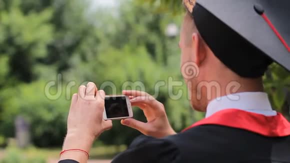 穿着学术服装的人在手机上拍照毕业日视频的预览图