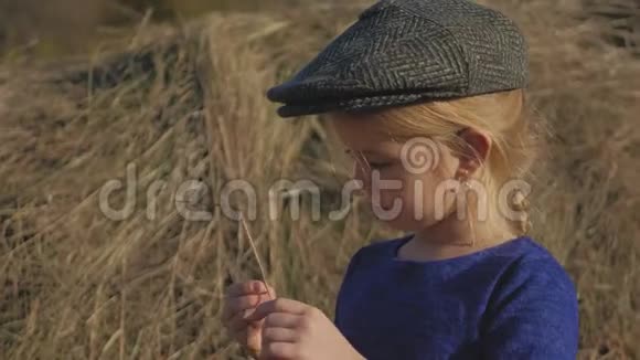 年轻可爱的女孩带着帽子玩得很开心坐在干草堆里用电话坐在干草上的小女孩视频的预览图