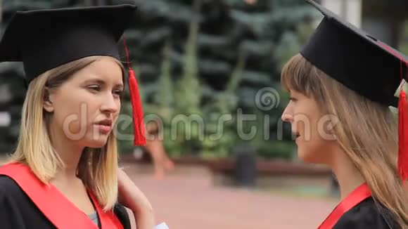 年轻的美女穿着学术服装在大学附近聊天毕业视频的预览图