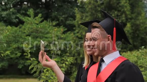 微笑的男女毕业生持有文凭和自拍电话视频的预览图