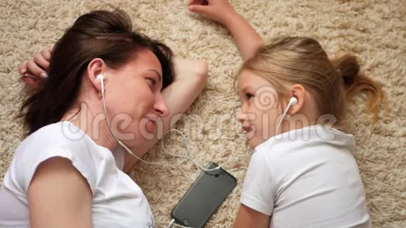 有趣的画面年轻女子和小女儿躺在地板上互相看着对方听着音乐视频的预览图