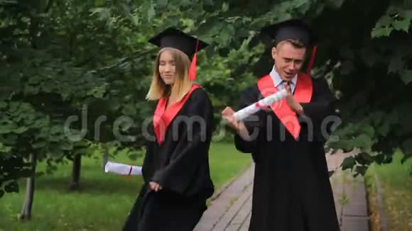 快乐的年轻毕业生在学院附近的公园跳舞庆祝毕业视频的预览图