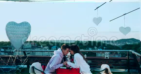 年轻的一对爱笑的情侣在装饰着屋顶的浪漫约会中轻轻地牵着手揉着鼻子视频的预览图