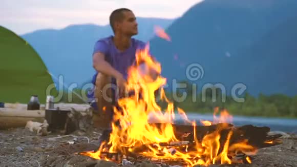 一位游客坐在山湖岸边的火炉旁视频的预览图