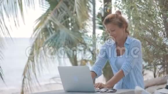 年轻女子坐在桌子旁手提电脑后面放着海景镜头移动视频的预览图