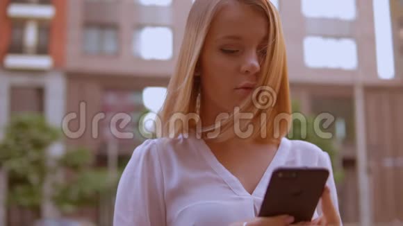 年轻的金发女人使用智能手机视频的预览图