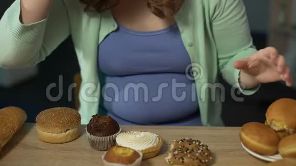 肥胖的年轻女人贪婪地吃着糕点吃着不健康的脂肪食物视频的预览图