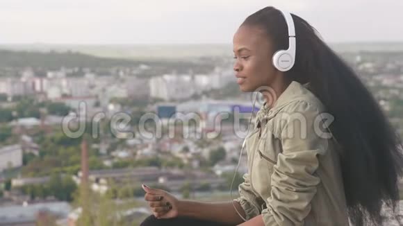 可爱的非裔美国女孩听音乐微笑美丽的黑人女孩户外城市景观背景视频的预览图