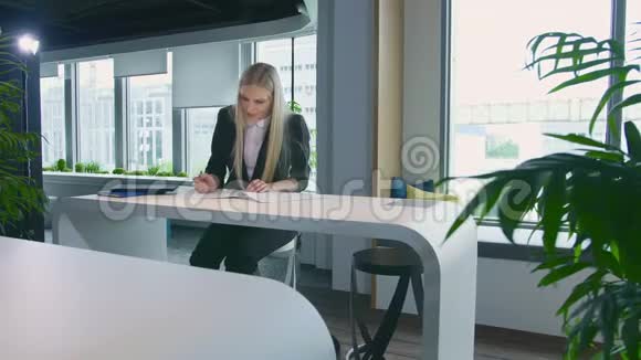 优雅的女人在时尚的办公室工作现代金发女郎穿着时髦西装坐在灯光下的办公室里视频的预览图