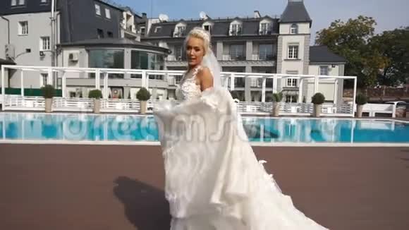 美丽的金发新娘穿着漂亮的婚纱在游泳池附近跳舞和旋转视频的预览图
