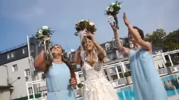美丽微笑的金发新娘和漂亮的伴娘们正在空中投掷婚礼花束并在附近接住视频的预览图