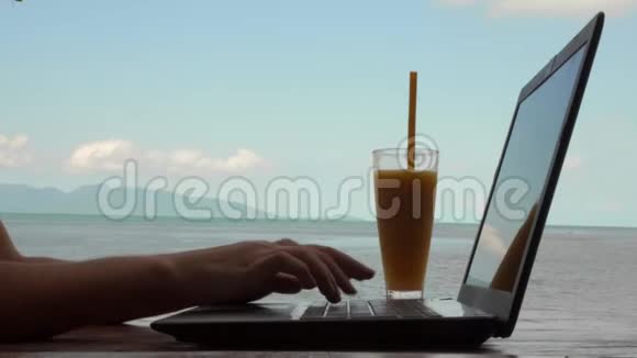 年轻的高加索女人使用笔记本电脑和饮用芒果水果奶昔与海景远程工作和自由职业概念视频的预览图