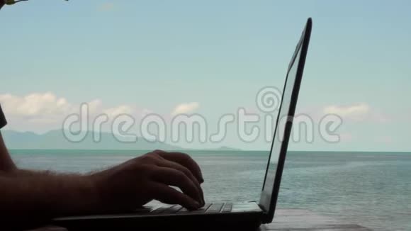 一个年轻的高加索人用的是带海景的笔记本电脑远程工作和自由职业者概念男性手靠近视频的预览图