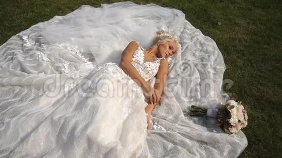 上图是一位年轻迷人的金发新娘躺在草地上温柔地抚摸着她的手臂视频的预览图