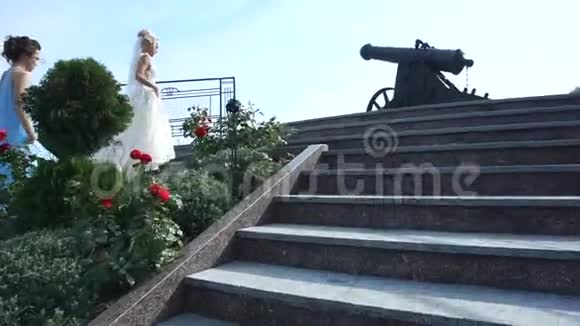 迷人的金发新娘和她的两个穿着蓝色连衣裙的伴娘正在室外上楼梯视频的预览图