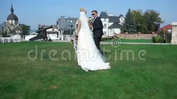 这对年轻漂亮的新婚夫妇手牵着手沿着城堡附近的花园散步视频的预览图