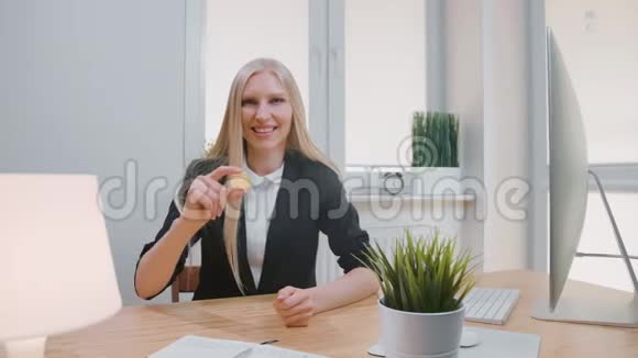 有比特币的快乐女性竖起大拇指穿着办公室西装的金发女郎微笑着坐在工作场所视频的预览图