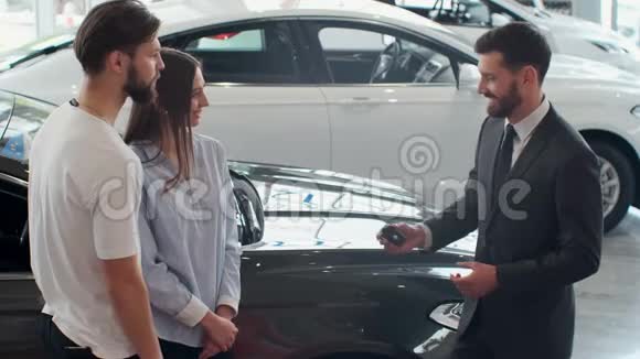 汽车销售员和年轻夫妇在汽车经销商的成功交易视频的预览图