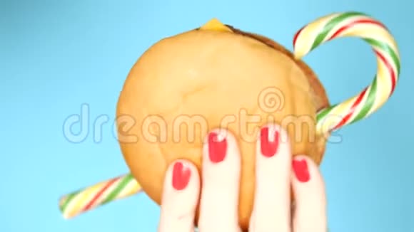 女性手拿着指甲拿着一个汉堡和棒棒糖在蓝色背景上特写视频的预览图