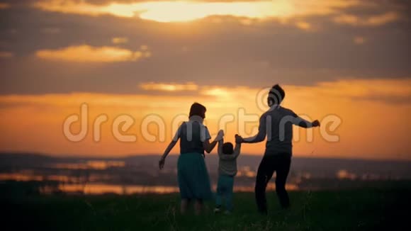 一家人牵着手爸爸妈妈在空中养育孩子一家人玩得很开心橙色的日落夏天视频的预览图