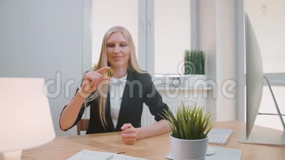 有比特币的快乐女性竖起大拇指穿着办公室西装的金发女郎微笑着坐在工作场所视频的预览图
