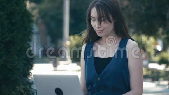 在城市街道背景长凳上的公园里用笔记本电脑工作的年轻女孩视频的预览图
