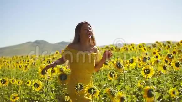 一个穿着黄色衣服的年轻女孩穿着向日葵穿过田野慢动作视频的预览图