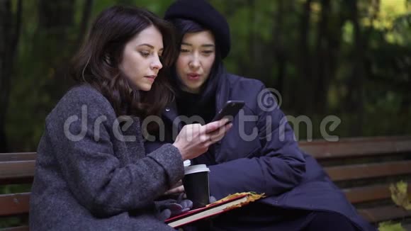 公园里有两个漂亮的年轻女人带着智能手机视频的预览图