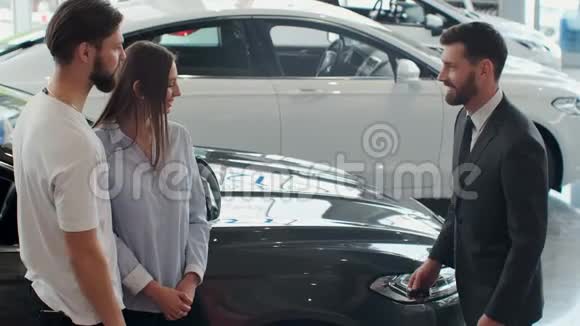 汽车销售员和年轻夫妇在汽车经销商的成功交易视频的预览图