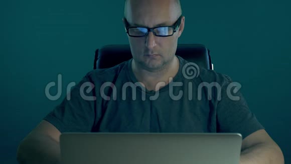 成年白种人无胡子的男性商人晚上在电脑上工作穿着时尚眼镜和T恤的男人视频的预览图
