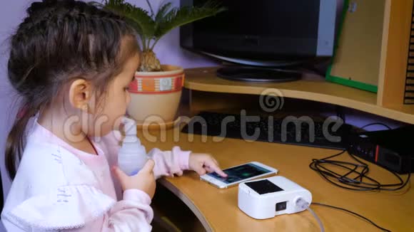 小可爱的女孩接受雾化器治疗并使用手机视频的预览图