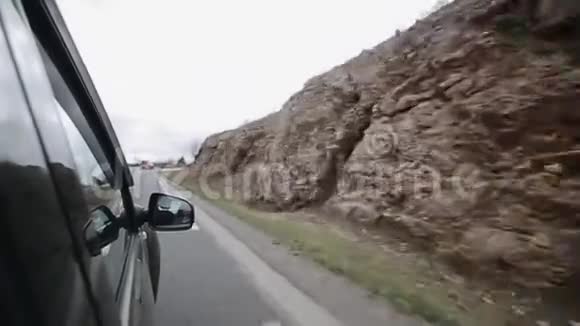一辆汽车在小山附近的一条弯曲的路上行驶翼镜中年轻女乘客的反映视频的预览图