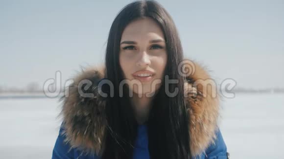 年轻开朗的黑发女子蓝夹克在冬天白雪皑皑的背景下微笑的肖像视频的预览图