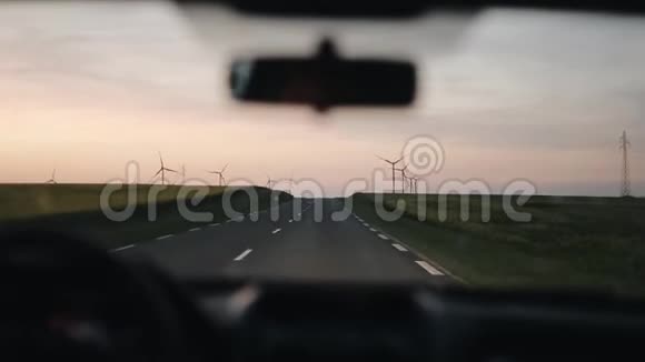 驾驶一辆汽车沿着乡村道路行驶两边都有风车和大田日落时分旅行视频的预览图