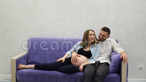 一对已婚夫妇正坐在家里的沙发上等待孩子的出生男人抚摸着她的手穿过她视频的预览图
