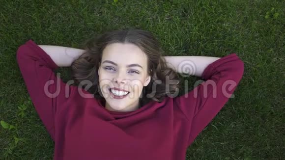 躺在草地上眨眼的年轻女子的俯视图视频的预览图