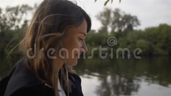 从侧面看一个女人听音乐沿着河走视频的预览图