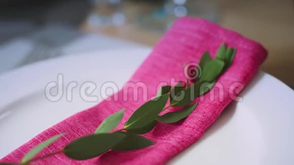 折叠的粉红色餐巾绿色的树枝躺在白色的盘子里视频的预览图
