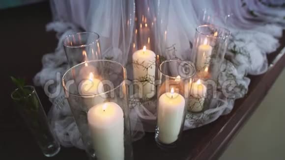 厚厚的燃烧着的蜡烛站在透明的花瓶里周围是由迪斯科舞厅灯光照亮的纺织品视频的预览图