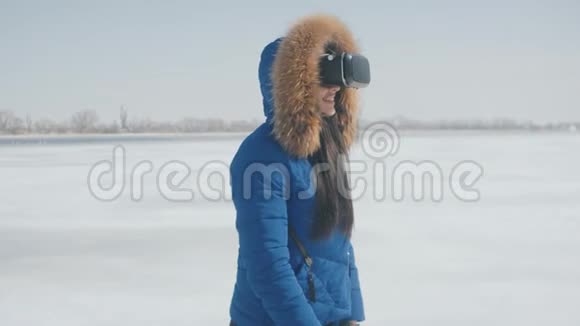 年轻女性蓝色夹克的肖像在冬季使用VR头套户外体验女孩使用虚拟视频的预览图