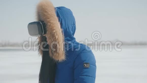 年轻的美女蓝夹克在冬天的雪背景下在户外使用VR耳机获得了经验视频的预览图