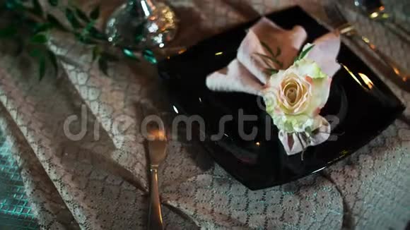 一个黑色的盘子上面放着一朵装饰的花和一张餐巾纸左右的餐具放在桌布上视频的预览图