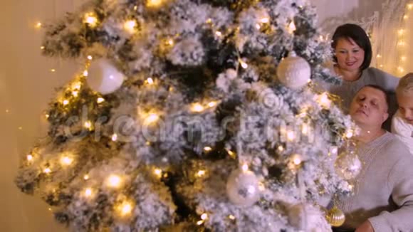 节日前夕在美丽的圣诞树上舒适的客厅里幸福的一家人视频的预览图