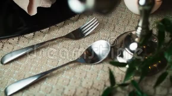 在黑色盘子右边的桌布上用勺子和叉子的特写镜头穿过烛台视频的预览图