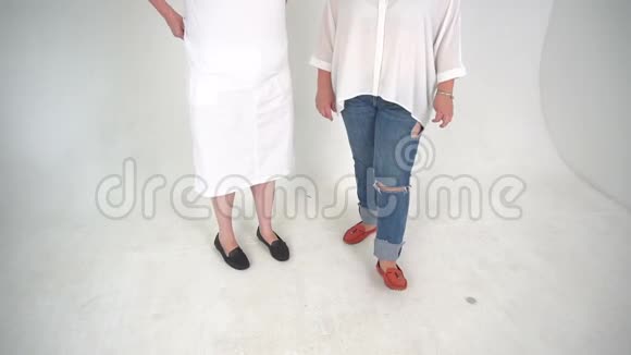 两个穿着牛仔裤和裙子的不可辨认的女人被隔离在白色背景的地板上视频的预览图