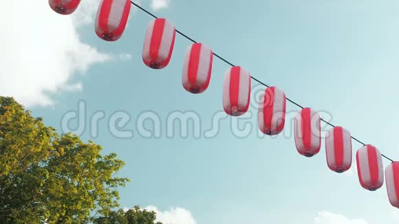 悬挂在蓝天背景和树木上的红白日本灯笼视频的预览图