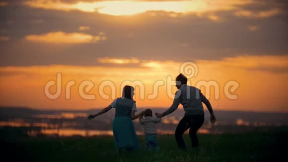 一家人牵着手爸爸妈妈在空中养育孩子一家人玩得很开心橙色的日落夏天视频的预览图